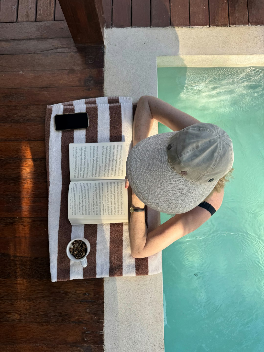 Person relaxing in a pool with a book and hat. Person relaxing in a pool with a book and hat.